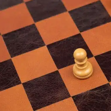 Pion en bois clair isolé sur l'échiquier en cuir marron et orange