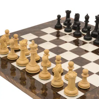 Ensemble d'échecs de luxe en ébène disposé sur échiquier en loupe de noyer